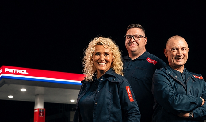 Na slici su tri osobe u radnoj odjeći sa Petrol oznakama. Stoje ispred Petrol benzinske stanice, dok su u pozadini vidljivi nadstrešnica, svjetla stanice i Petrol logotip.