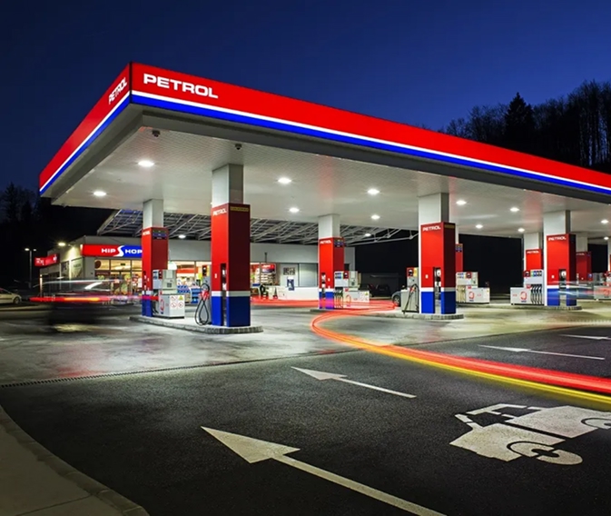Petrolova benzinska stanica noću s osvijetljenim točionicama, prodavnicom i svjetlosnim tragovima vozila.