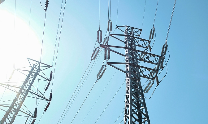 Na slici su visokonaponski dalekovodi i električni stubovi sa provodnicima. Konstrukcije se uzdižu prema vedrom plavom nebu, a električni vodovi povezani su između stubova.