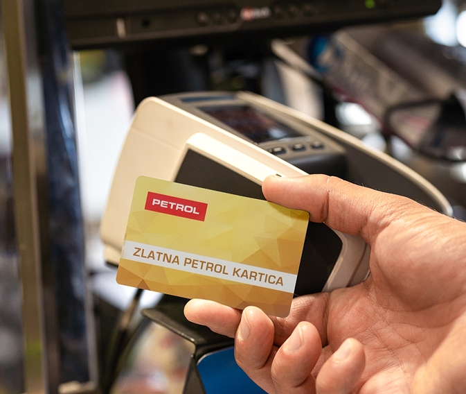 Ruka drži Zlatnu Petrol karticu ispred platnog terminala.